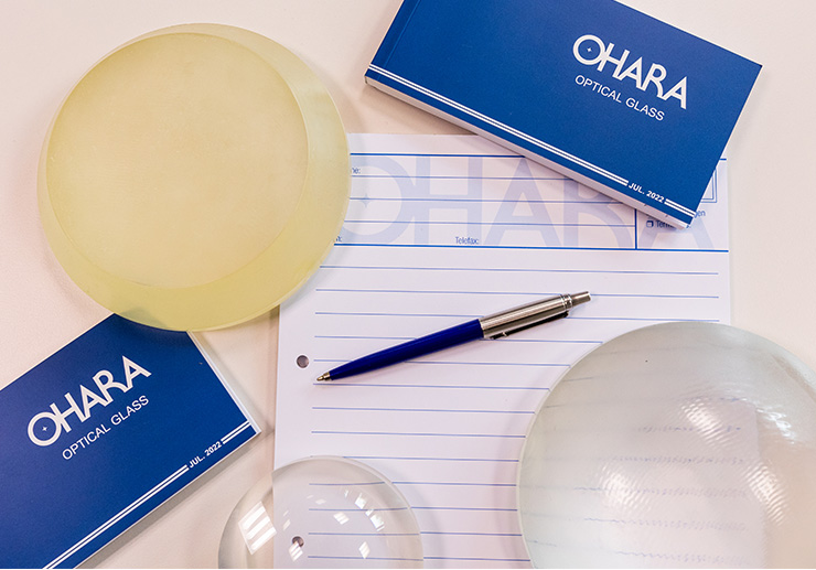 Auf einem Tisch liegen zwei OHARA-Broschüren, ein OHARA-Notizblock, ein Kugelschreiber und drei Glas-Rohlinge.
